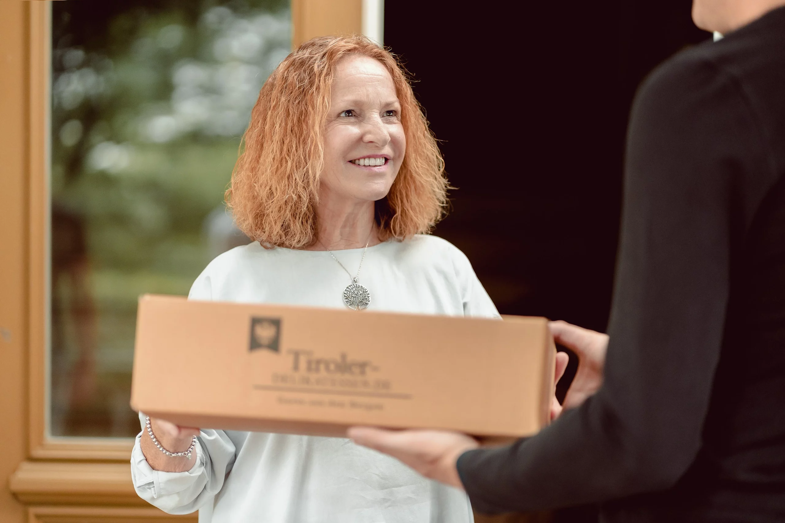 Frau nimmt lächelnd eine Geschenkbox von Tiroler Delikatessen entgegen