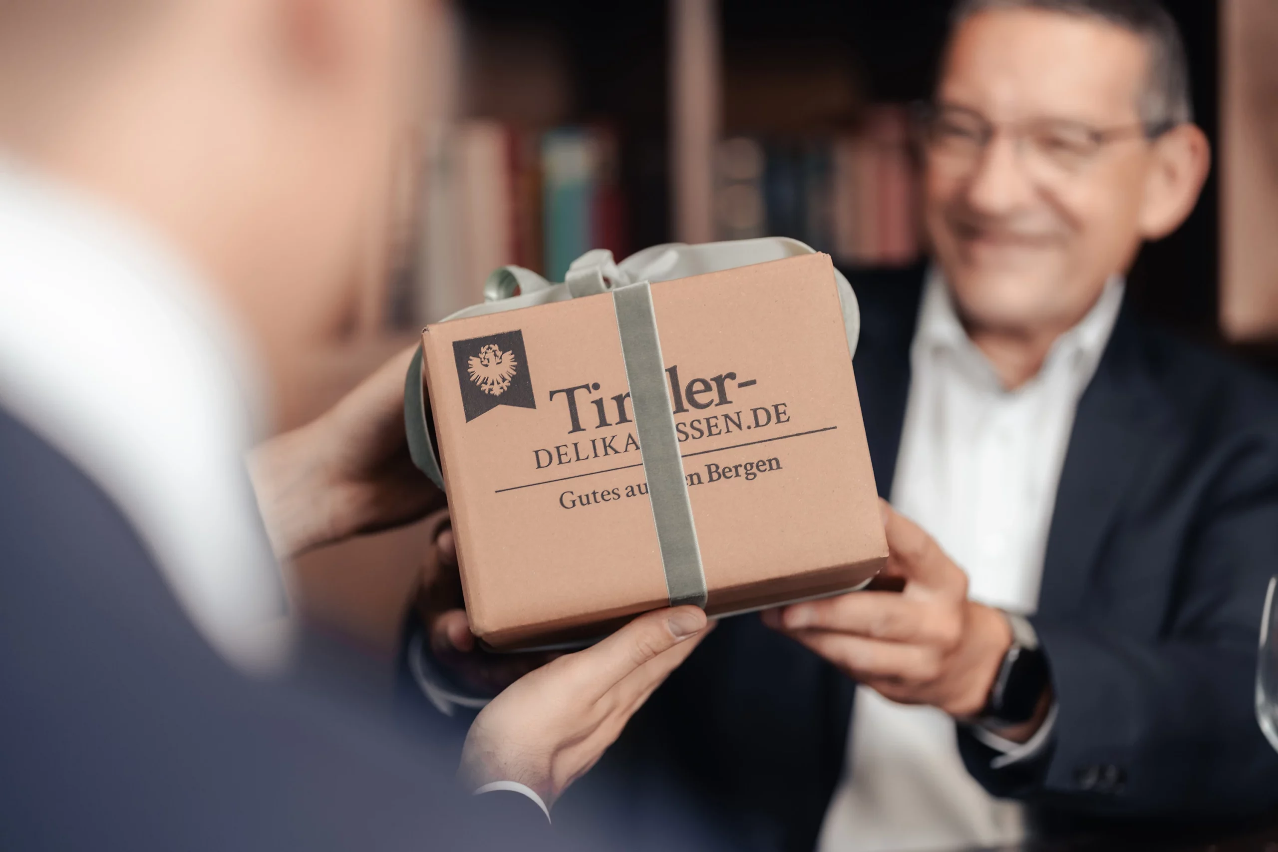 Mann im Anzug überreicht eine Geschenkbox von Tiroler Delikatessen