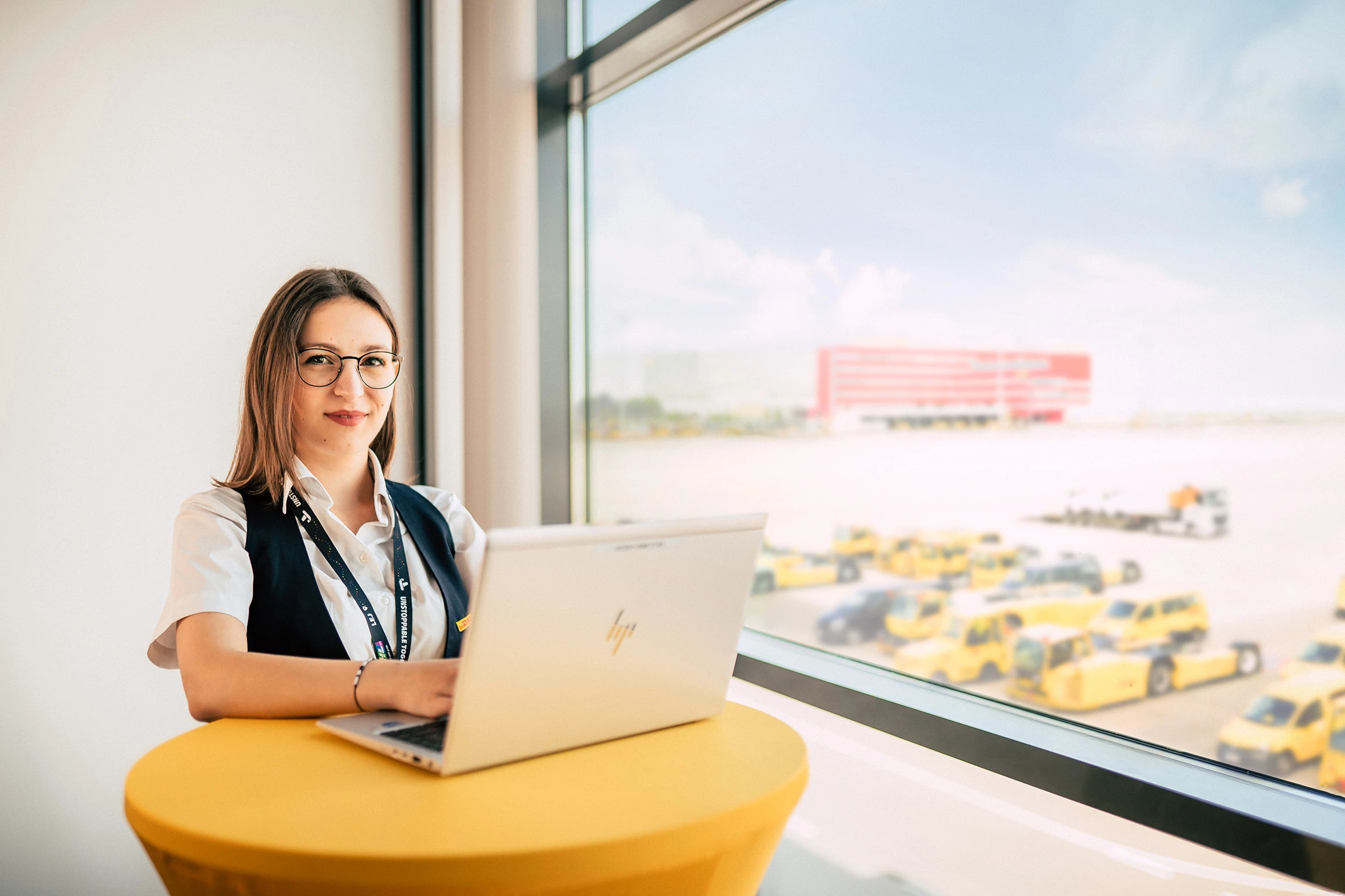 Mitarbeiterin arbeitet lächelnd am Laptop vor einer großen Fensterfront