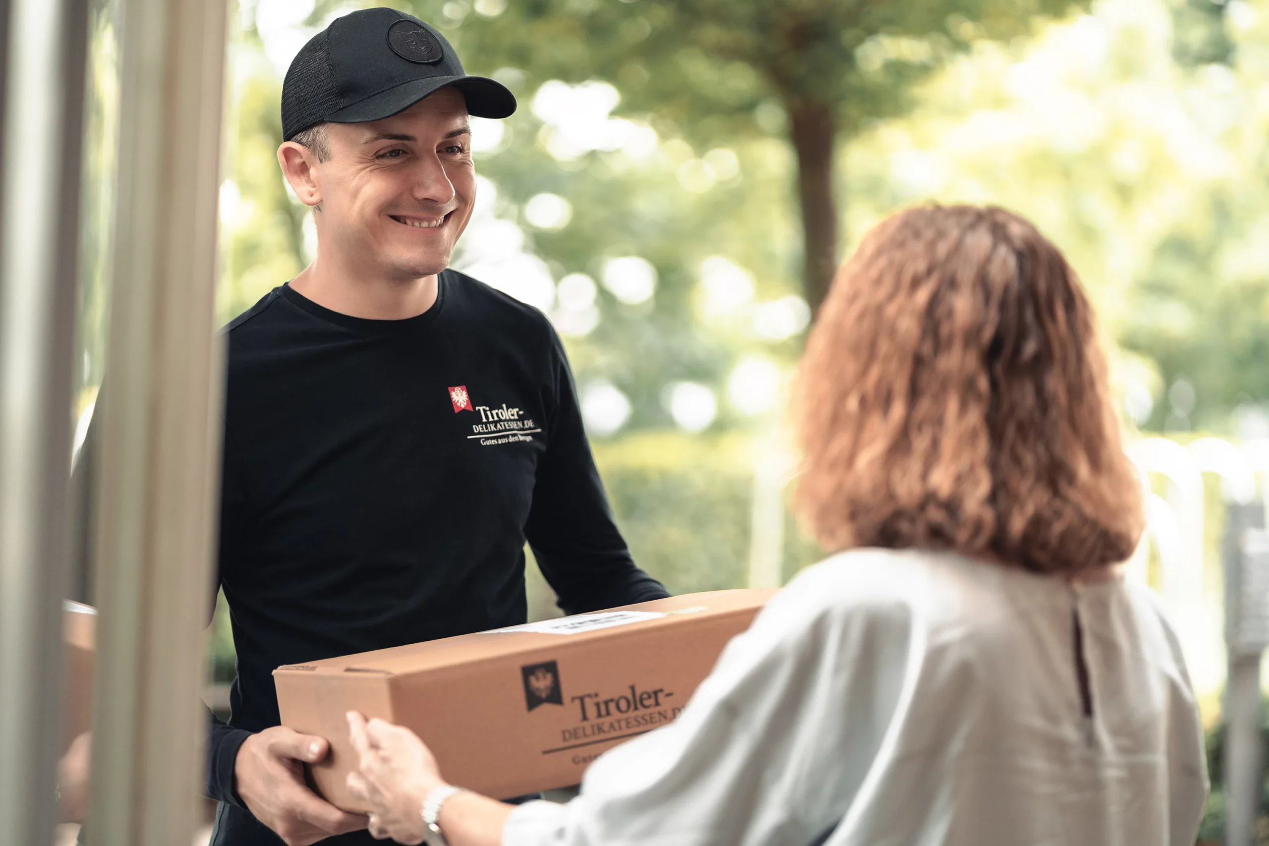 Mitarbeiter von Tiroler Delikatessen überreicht einer Kundin eine Geschenkbox