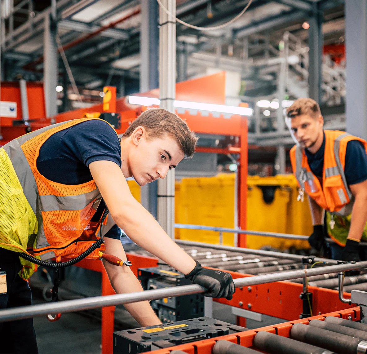 Zwei Mitarbeiter in Warnwesten arbeiten an einer Rollenbahn im Logistikzentrum