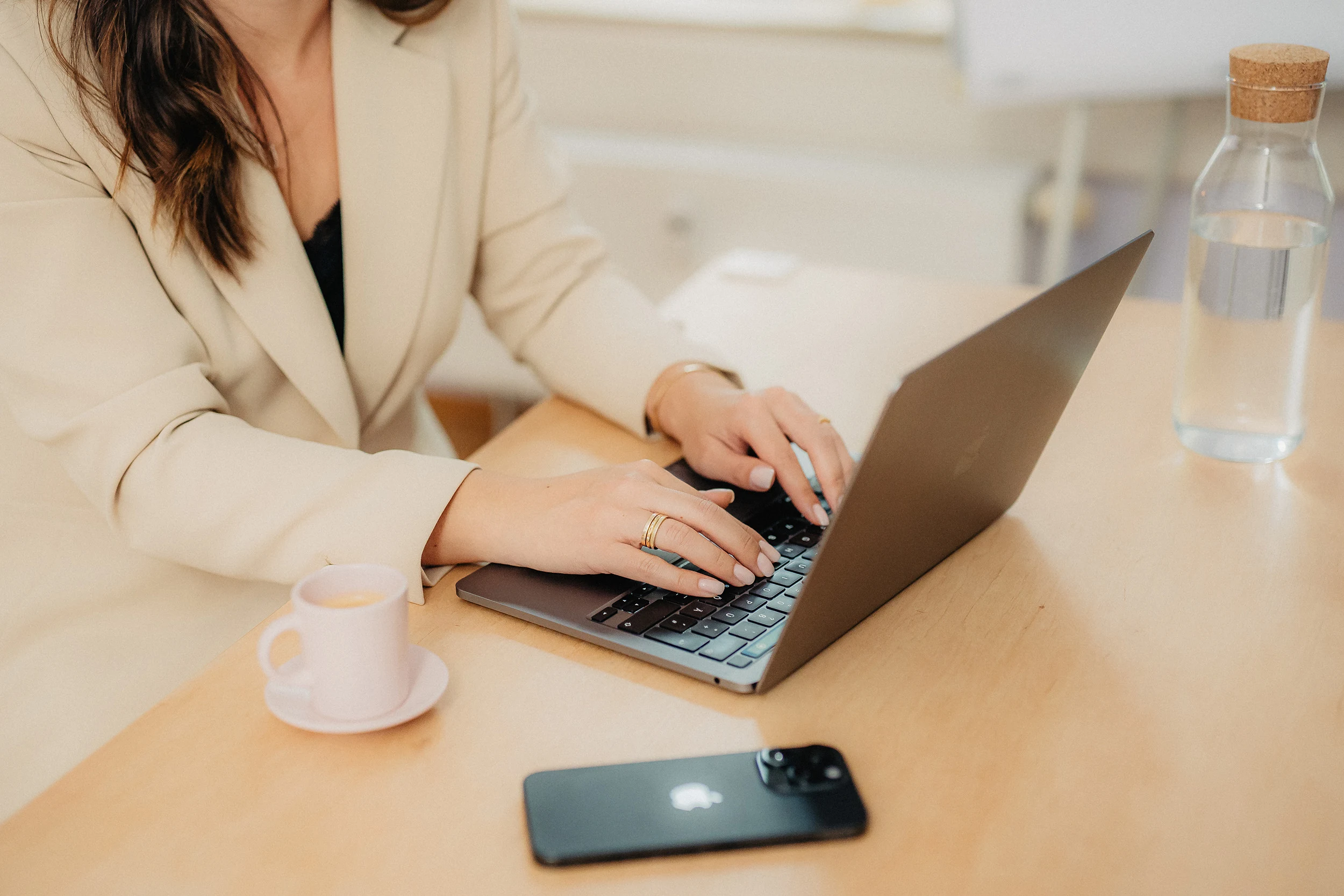 Hände auf der Tastatur eines Laptops, daneben Smartphone und Kaffeetasse