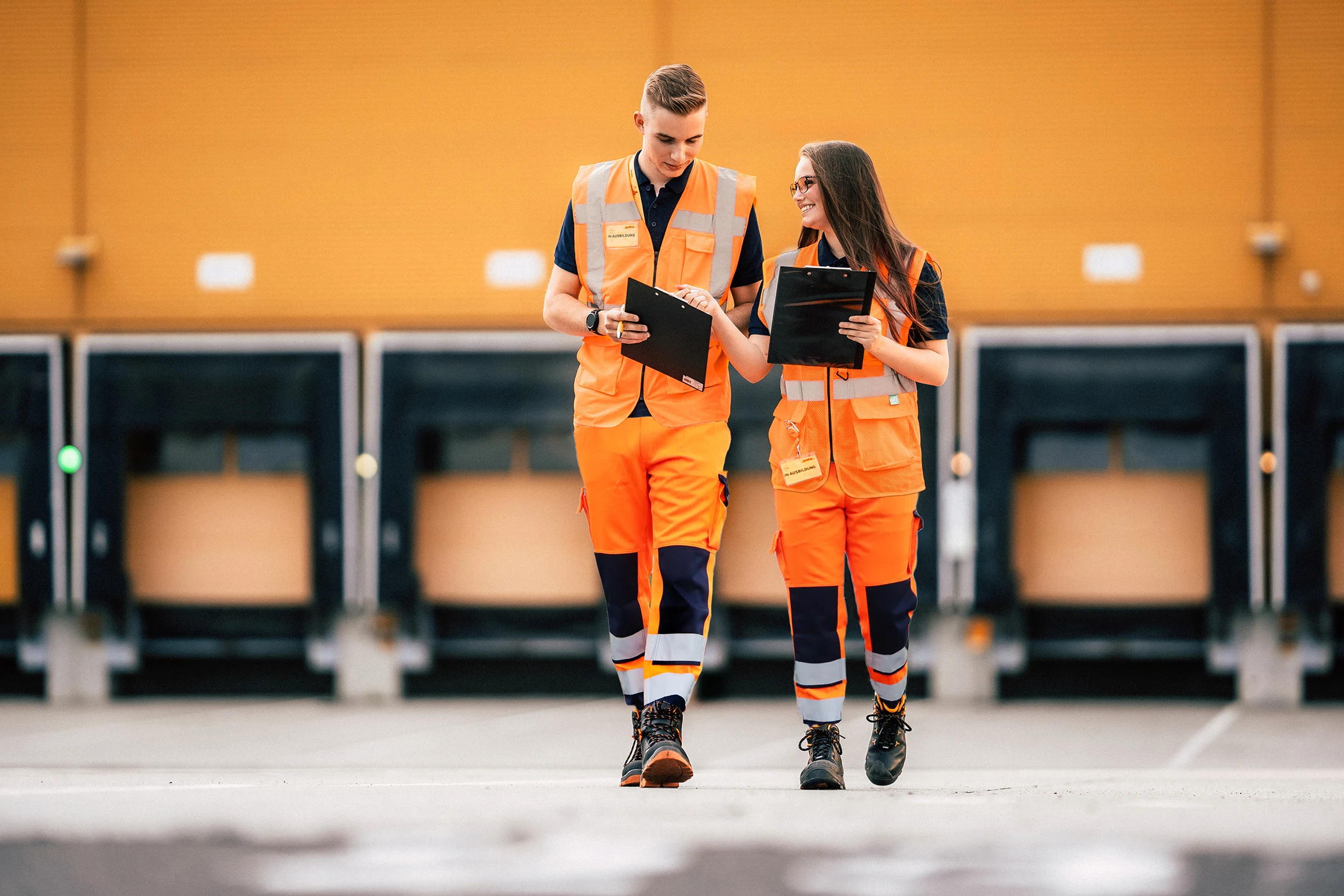Zwei Mitarbeitende in Warnkleidung vor den Verladetoren bei DHL
