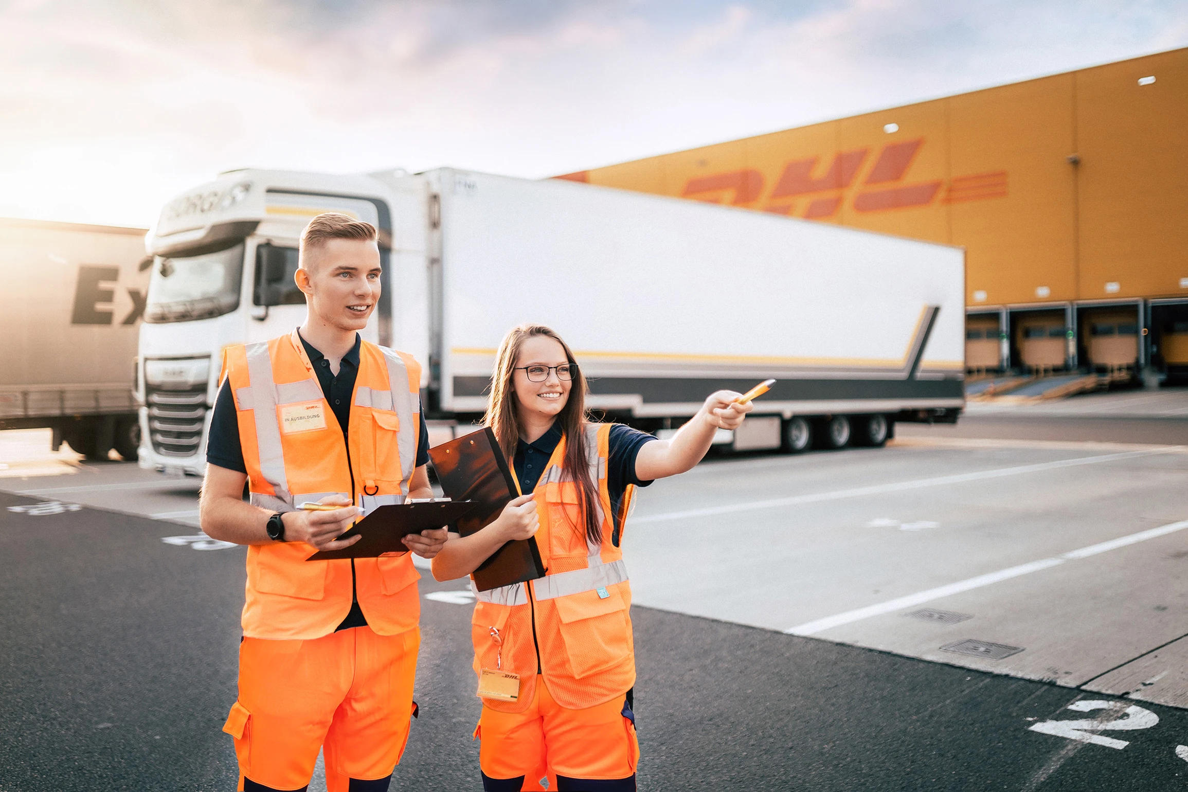 Zwei Mitarbeitende in Warnwesten mit Tablet vor einem DHL-Lkw